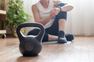 Are Kettlebells a Hack for Triathlon Strength Training? Mature woman sitting on a yoga mat, checking her fitness tracker after an authentic home workout, focusing on health, wellness, and a sustainable lifestyle, with a kettlebell in the foreground