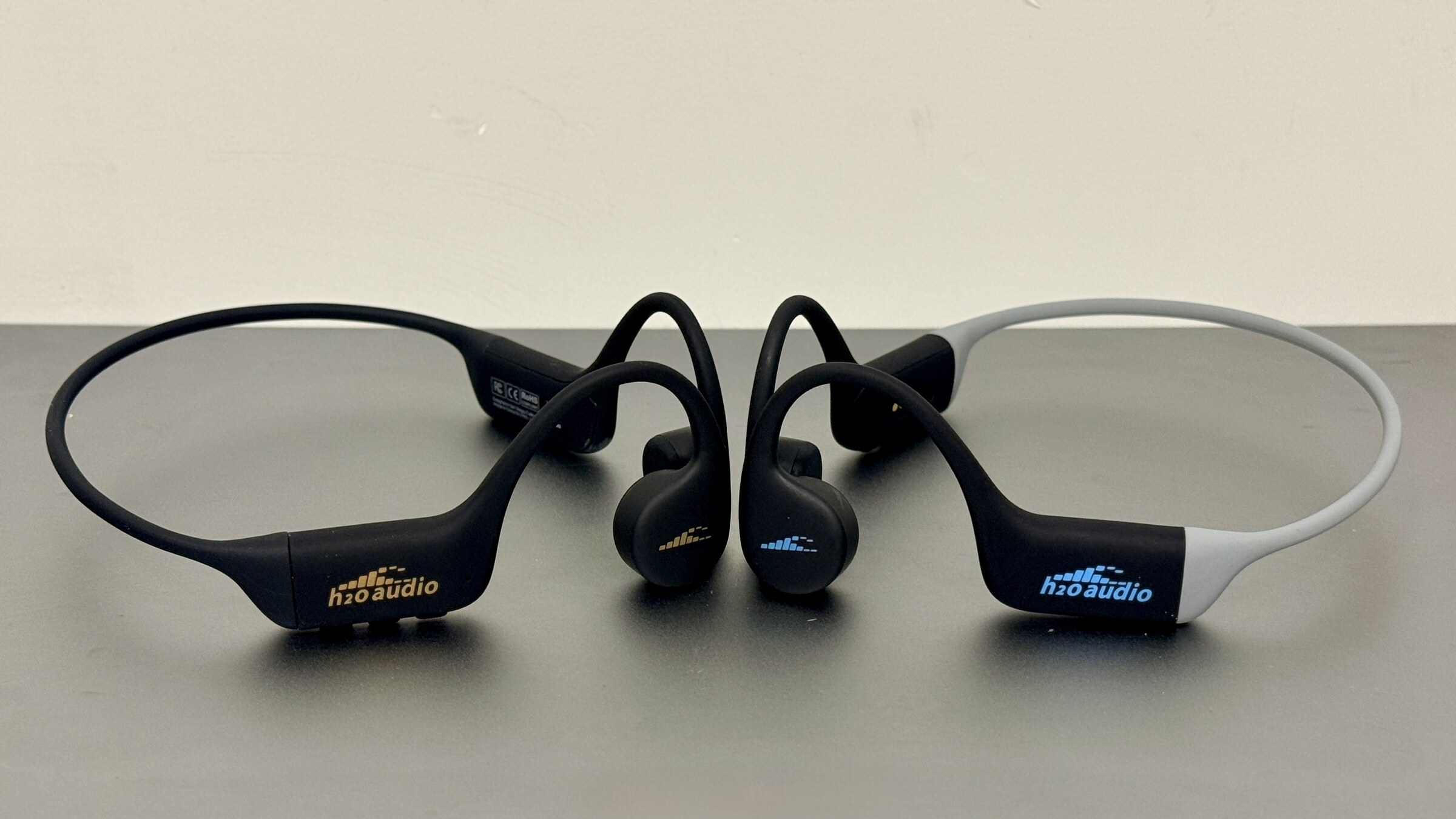 H2O Audio TRI 2 PRO and TRI Run bone conduction headphones side by side on a bench.