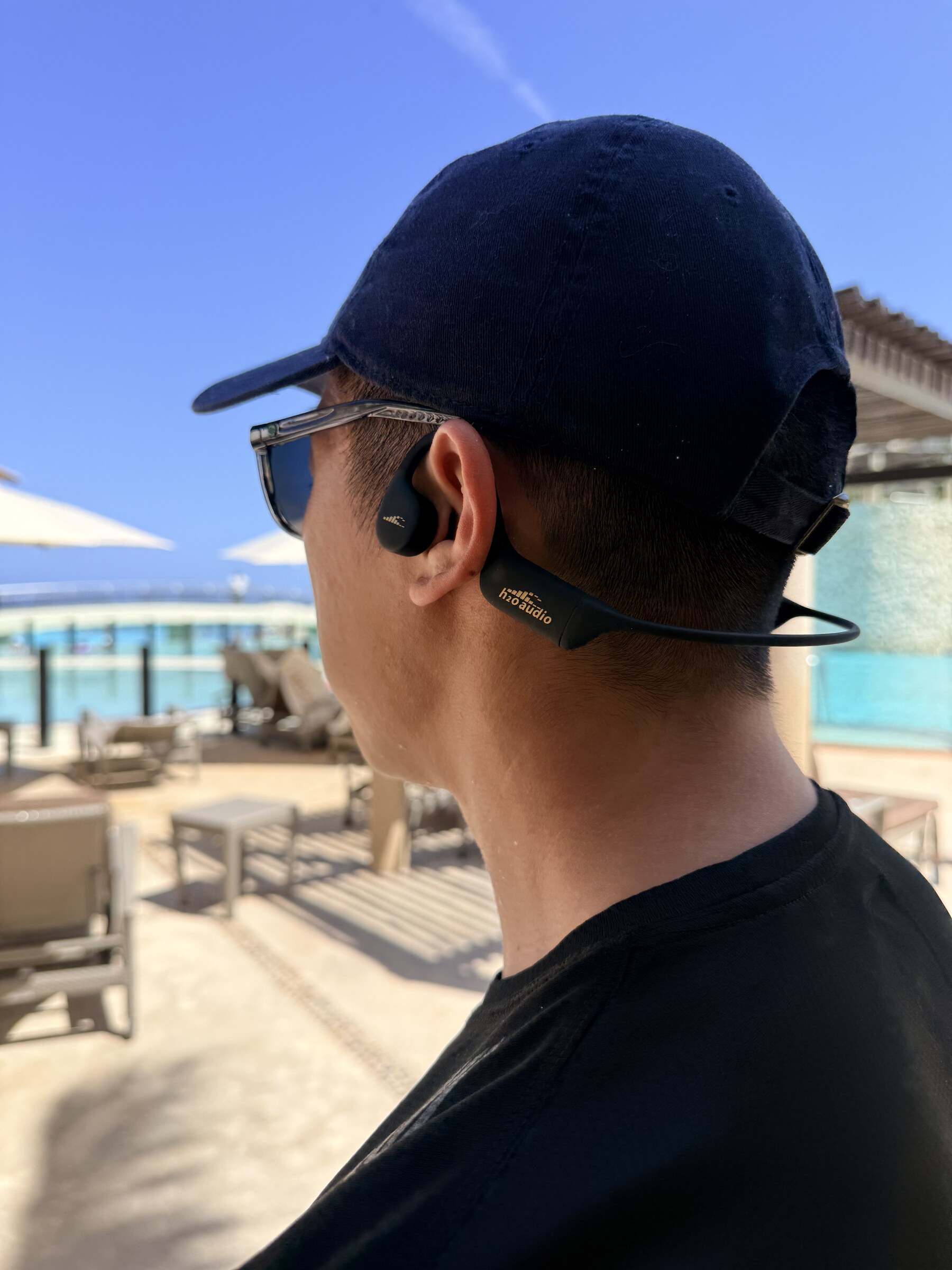 Rear three-quarter view of the H2O Audio TRI 2 PRO showing the wraparound band sitting low behind the head under a cap.