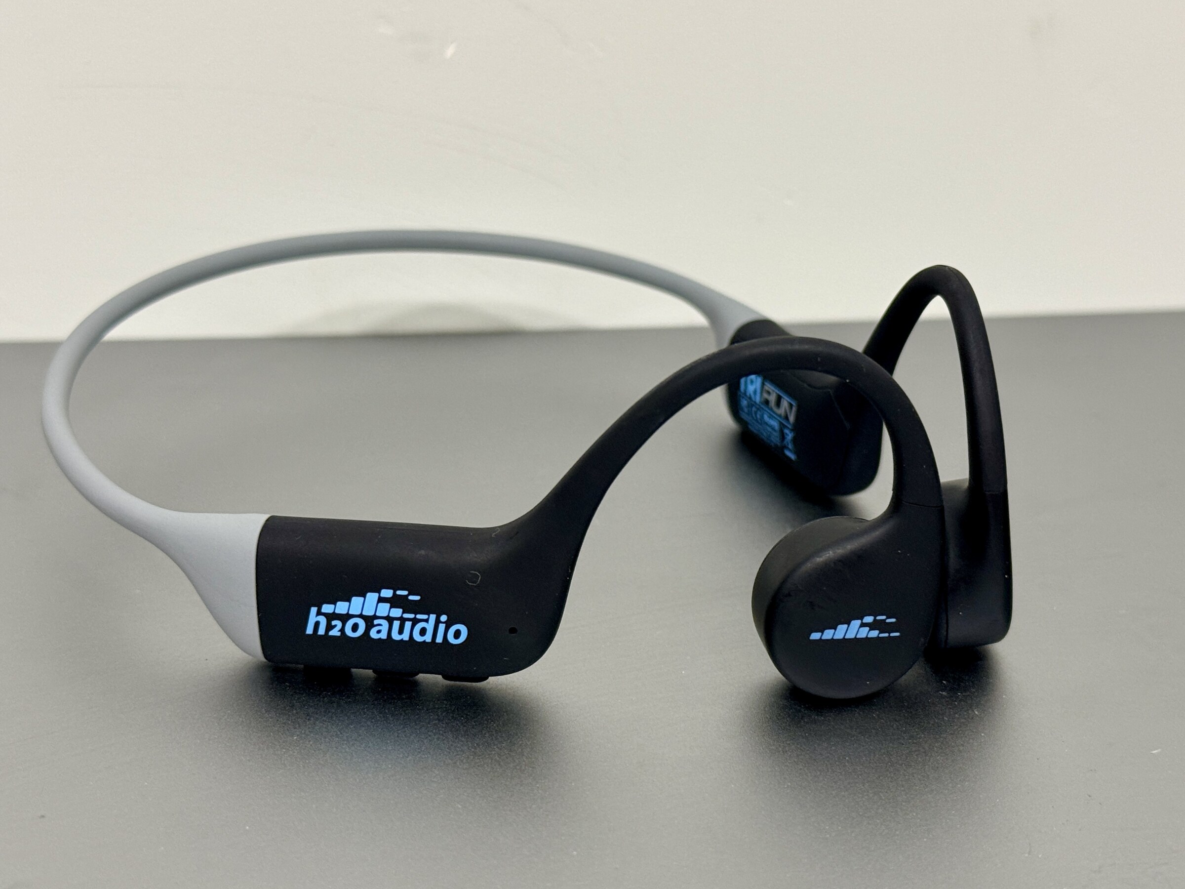 H2O Audio TRI Run bone conduction headphones in the black and gray colorway, photographed on a bench.