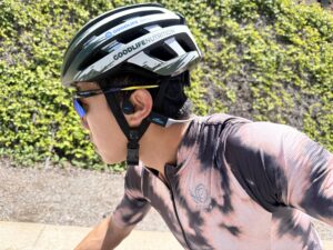 Close-up of the H2O Audio TRI Run bone conduction headphones worn under a cycling helmet, with the ear canal left completely open.